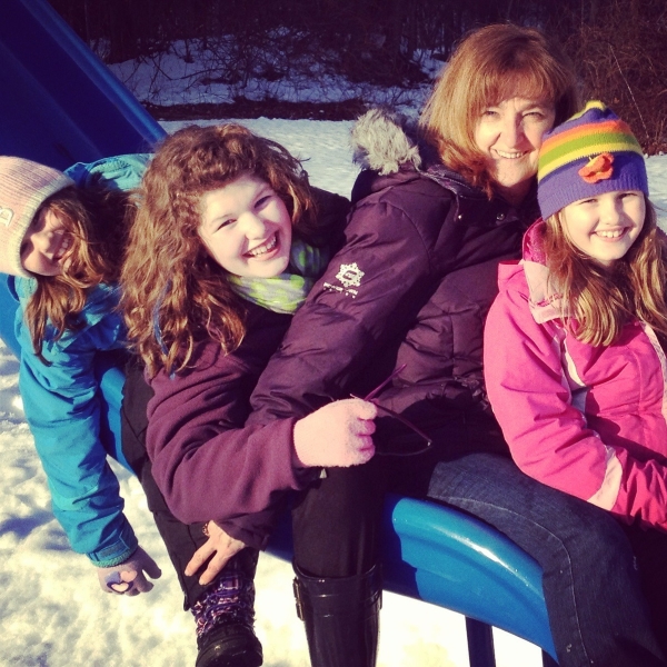 Pat Lightizer photo with grandkids riding a slide in the park in winter, snow on the ground and all bundled up with winter coats and hats